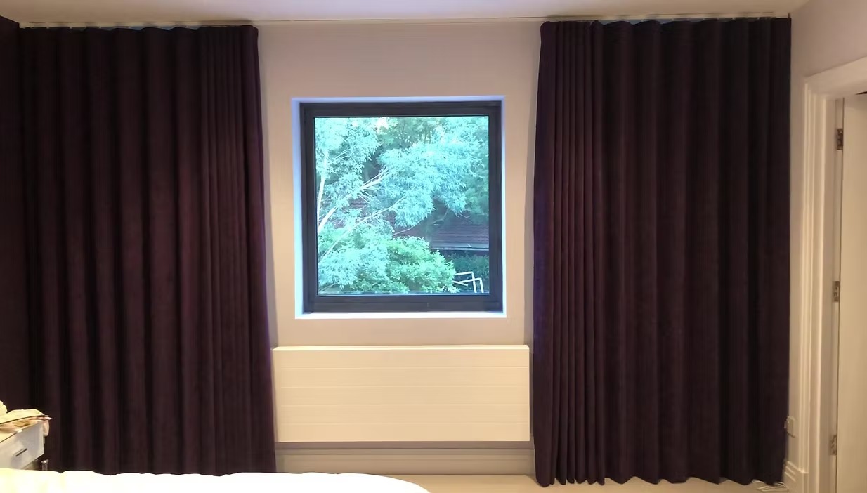 Dark pleated bespoke bedroom curtains framing a window above a radiator