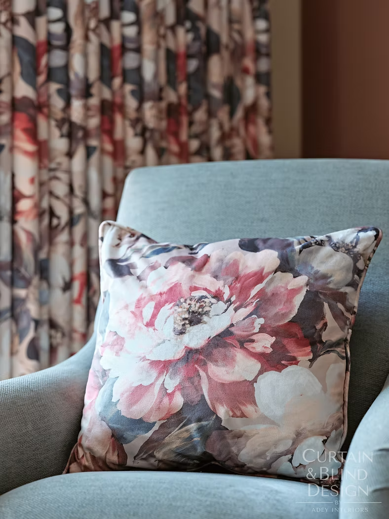 Pale blue reupholstered chair with a floral cushion beside patterned curtains