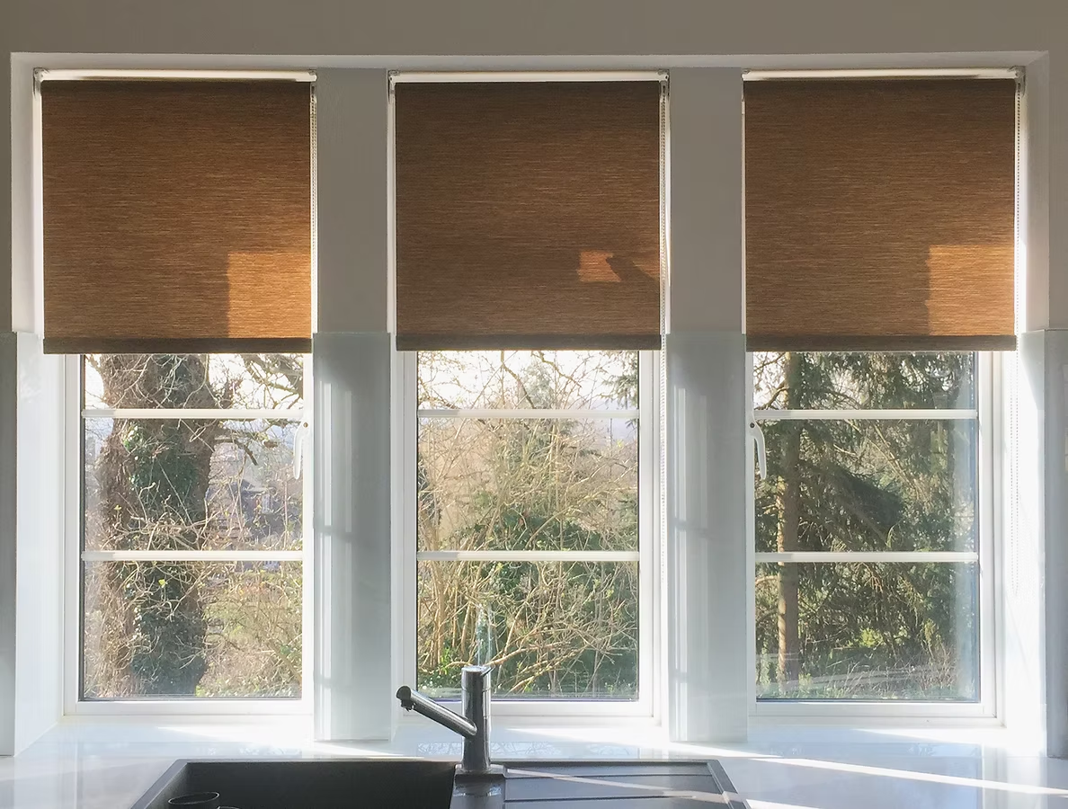 Woven roller blinds fitted to three sash windows above a kitchen sink