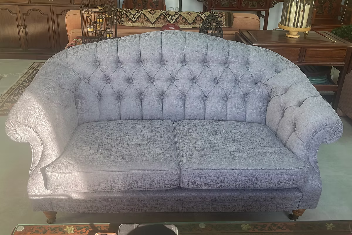 Pale grey button-tufted sofa reupholstered with rolled arms in a traditional room