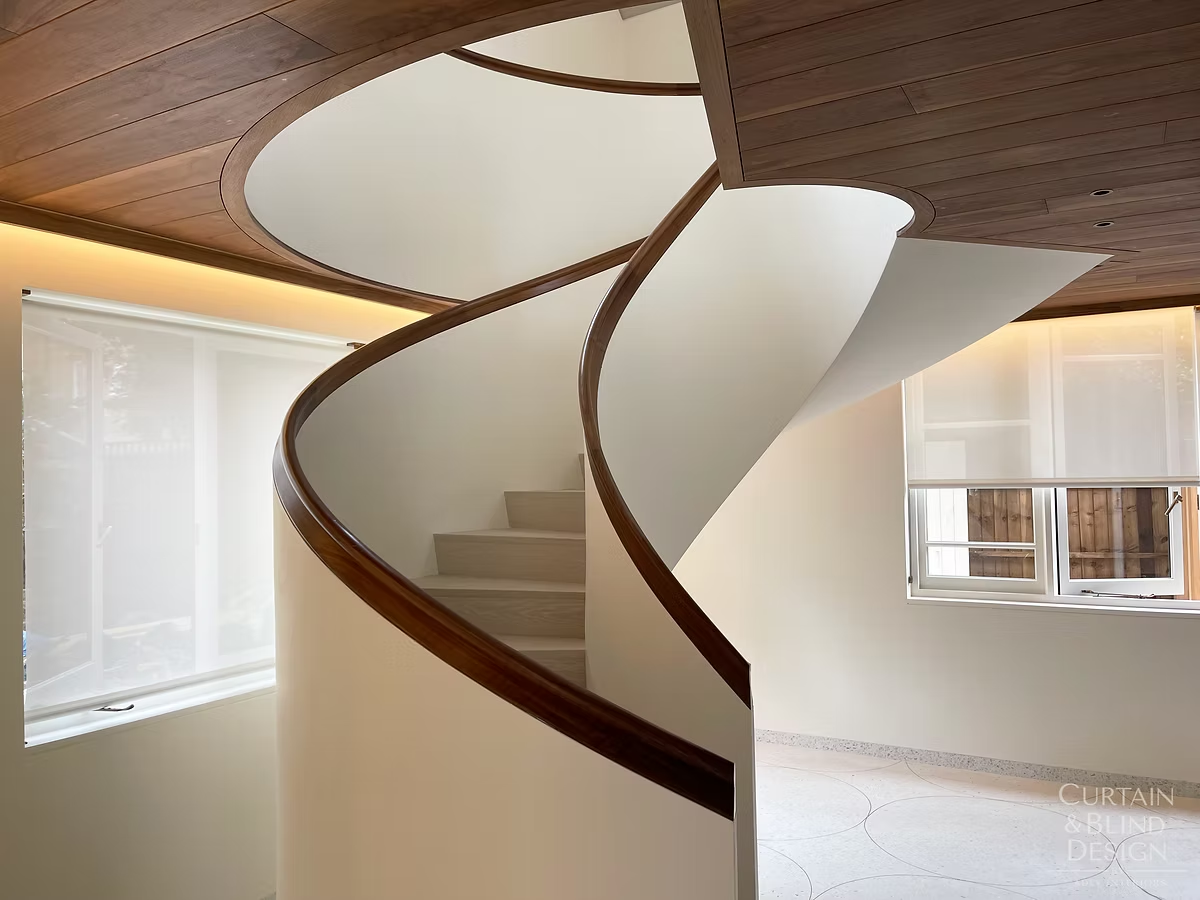 Roller blinds fitted to stairwell glazing above a curved wooden spiral staircase