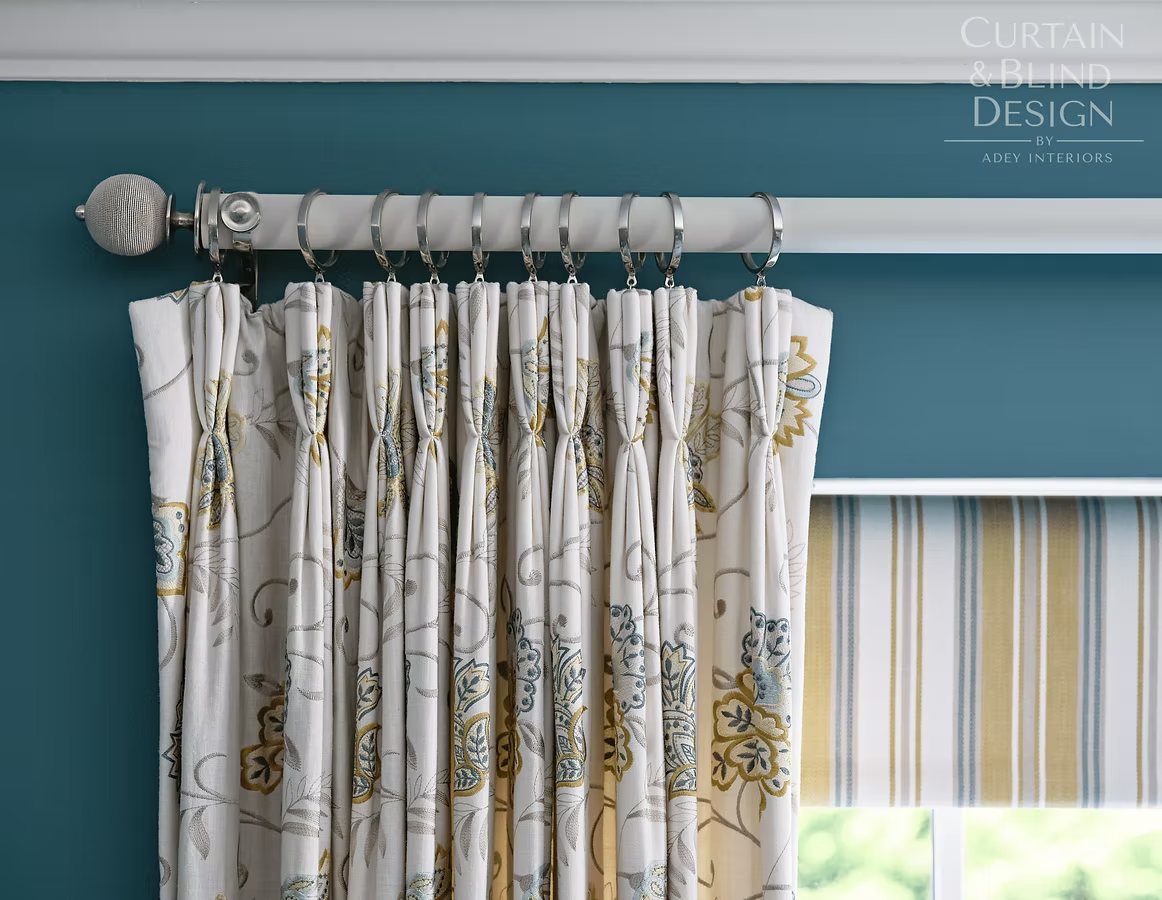 Patterned curtains hung on a white curtain pole against a teal bedroom wall