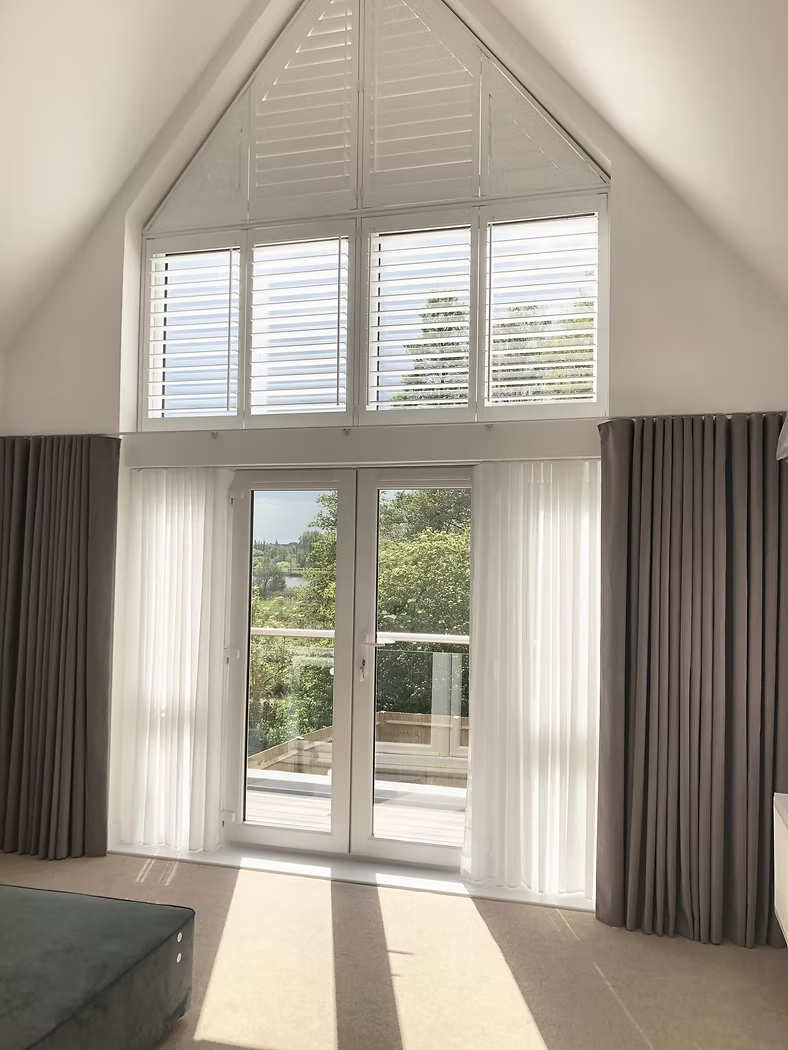 Layered window dressing scheme with shutters, sheer curtains and full-length side curtains to an apex window
