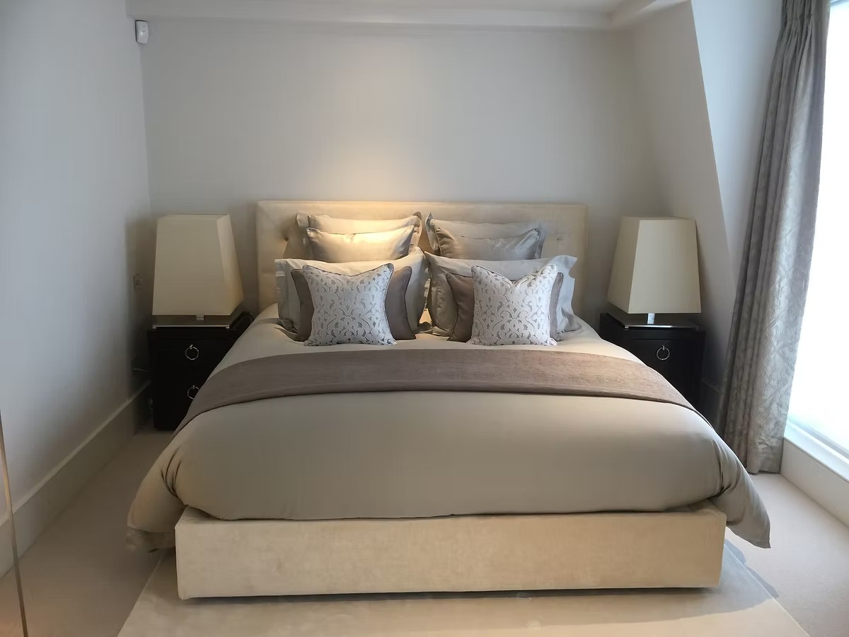 Cream upholstered bed with layered scatter cushions in a neutral bedroom