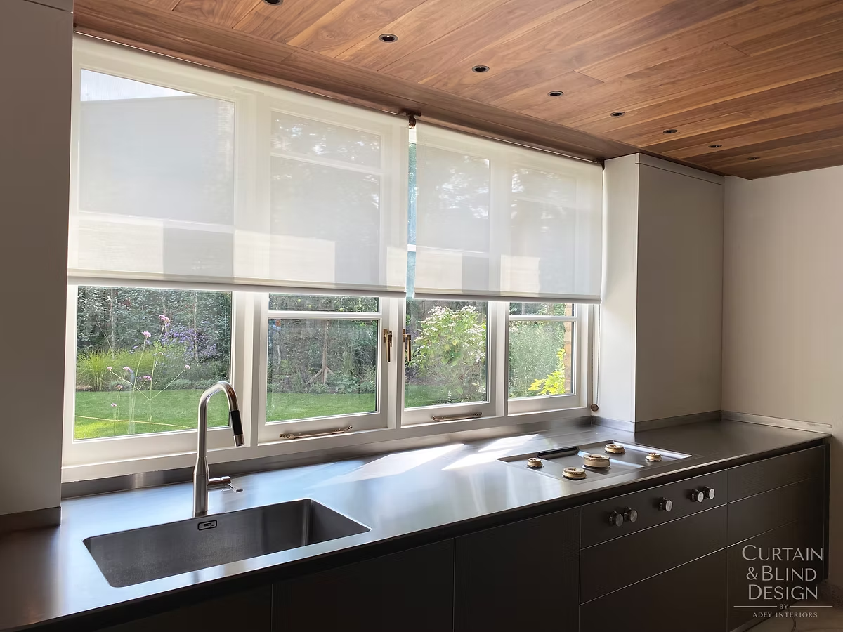 White roller blinds fitted across a run of kitchen windows with garden views