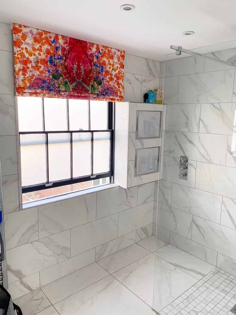 Bold floral Roman blind fitted to a black-framed window in a marble bathroom
